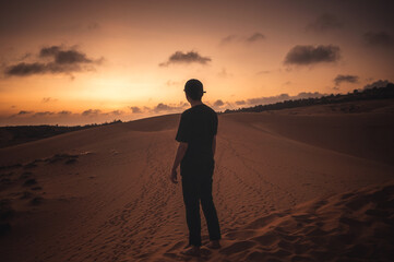 Traveler man with cap standing on dune at sunset