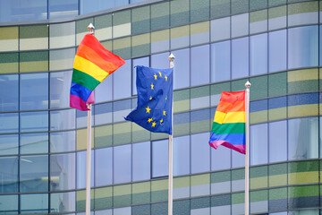 The Pride flags and European Union flag on white flagpoles against the modern building.