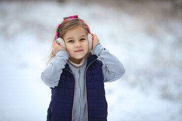 a little girl in warm headphones walks in the winter in a snowy Park and holds her head with her hands. hardening of children.