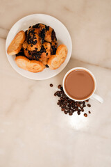 Cup of coffee, coffee beans, with plate of sweets on marble table, top view