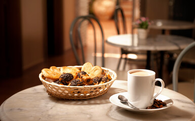 cup of coffee, on marble table, with pastries in wicker basket, cafeteria tables background