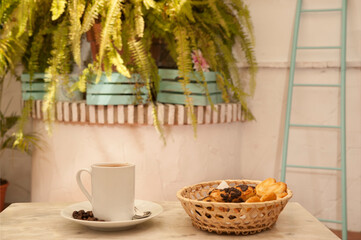 cup of coffee on marble table, with pastries in wicker basket, and Mediterranean house background with plants