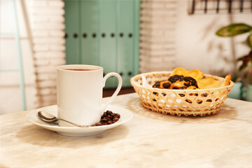 cup of coffee on marble table, with pastries in wicker basket, and Mediterranean house background with plants