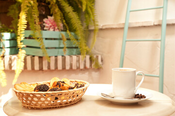 cup of coffee on marble table, with pastries in wicker basket, and Mediterranean house background with plants