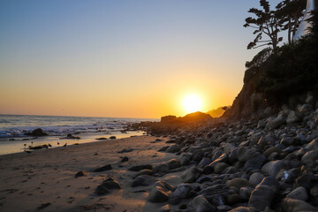 a stunning shot of the sunset and the ocean and the rock and people walking on the beach at El...