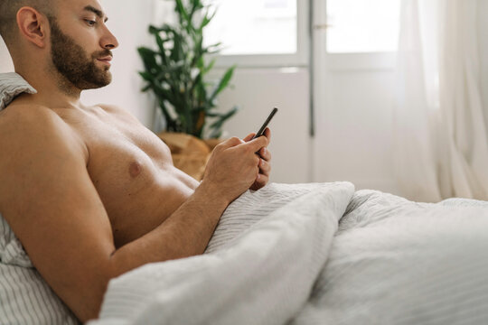 Young handsome man using his mobile phone in the bed