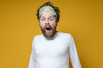 Shaggy, bearded man with a sleeping mask on his head yawns amusingly. Yellow background.
