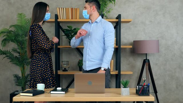 Man and woman wear protective medical masks on faces greet elbows employees working together in an office preparing presentation for meeting. Manager shows report to businesswoman on laptop computer
