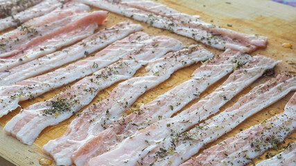 sliced raw bacon on a Board in spices. with pepper oil, herbs. delicious food.
