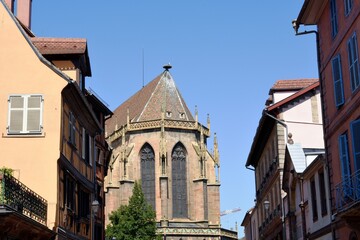 Narrow streets of medieval and early Renaissance buildings with window boxes draped with blooms in Colmar, town in the Grand Est region of northeastern France. On the background is St Martin's 
