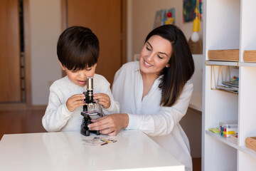 Kid exploring science with a microscope and mother or teacher help. Homeshooling. Learning Community. Montessori School