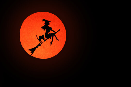 Dark Halloween background.Silhouette of a witch on a broom and her cat on the background of a round full moon in red.copy space.creepy mood