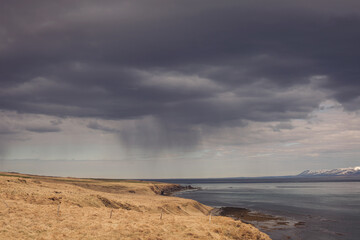 Sea landscape in Iceland. View of beach and mountain. The water is clear blue and low clouds dot the deep blue sky.