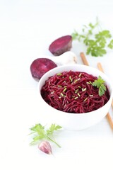 Korean beetroot salad with garlic and parsley in a bowl with wooden sticks on a white background