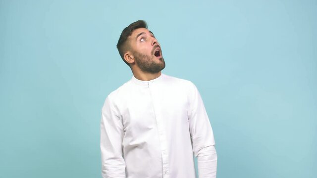 Young caucasian handsome man pointing up, looking surprised and amazed, is presenting a product