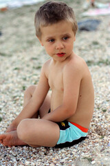 Cute boy 3-4 years old sits on the sand on the beach and looks into the distance