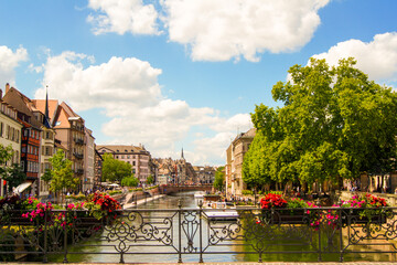Scenic view of the cityscape of Strasbourg, France with beautiful, colorful blooming summer flowers in flower boxes at a metal bridge railing in the front.