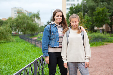 Pre-teen schoolgirl in grade 6 goes back to school at September with her mother, together portrait outdoor