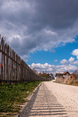 Wooden fence along the stony woodland path with dark shadows of the fence and cloudy sky