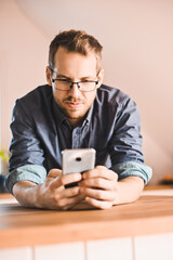 attractive nerd guy with glasses in stylish kitchen follows a recipe or  reads news on the phone