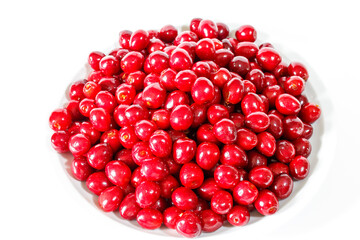 Red cherries lie in a white plate on a white background