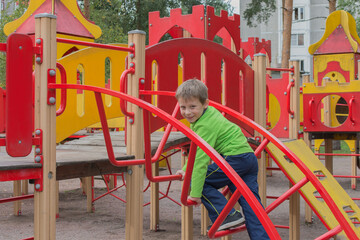 Fototapeta na wymiar A child climbs the stairs in an open playground in a summer park. Entertainment and play center in kindergarten or in the school yard. Concept - childhood, entertainment, sports