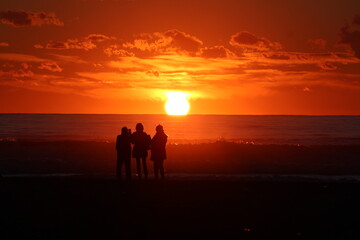 persone che ammirano il tramonto in riva al mare