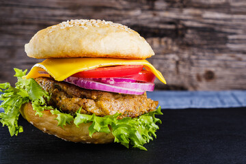 Fresh delicious homemade veggie burger lies on natural slate on rustic wooden background. Delicious tasty burger with lettuce, cheese, onion and tomato. buckwheat and lentil cutlet