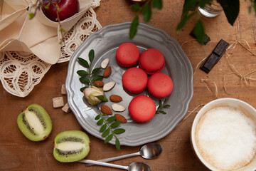 Five macaroons on a grey plate wuth almonds, chocolate and kiwi