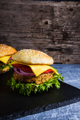 Two Fresh delicious homemade veggie burger lies on natural slate on rustic wooden background. Delicious tasty burger with lettuce, cheese, onion and tomato. buckwheat and lentil cutlet