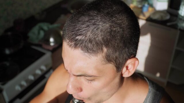 Young guy smokes an electronic cigarette at home. The man uses a vape. Bad habits. An alternative to tobacco