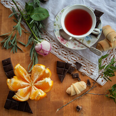 A cup of tea, orange and chocolate pieses on a wooden table