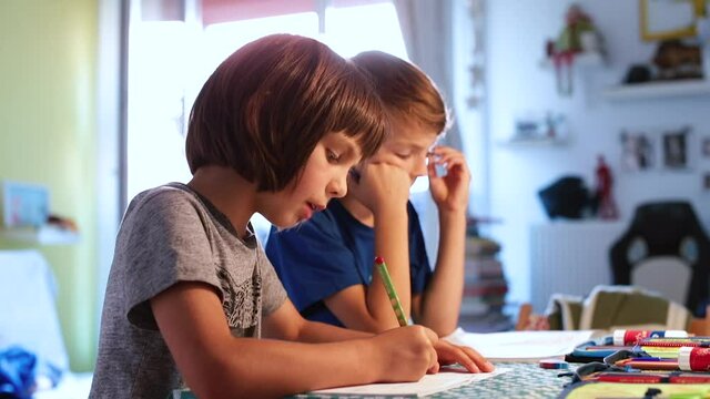 The boy chews gum and writes text in a notebook on the table. Self-fulfillment of tasks at home. Distance education outside of school.