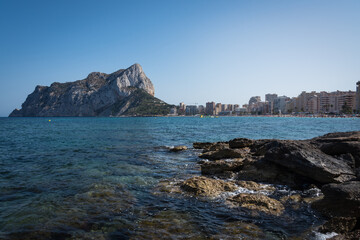 View from the rocks of the coastline with the urban beach of Calpe and the crag in the background, Alicante, Spain