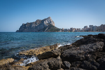 View from the rocks of the coastline with the urban beach of Calpe and the crag in the background, Alicante, Spain