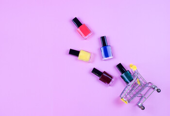 Different colors nail polishes and a shopping trolley on a pink background. beauty and fashion trendy concept. flat lay, top view