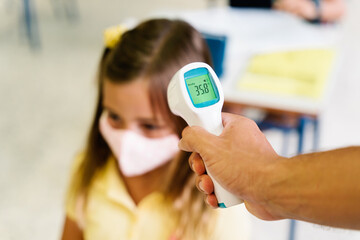teacher taking a girl's temperature with a thermometer during covid pandemic. 