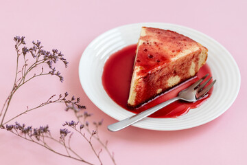 Cheesecake on a white plate with strawberry sauce, on a light pink background.