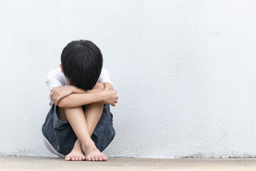 Fototapeta premium A boy sitting alone with sad feeling. Asian little child covered his face with his hands in fear. Domestic Family violence concept.