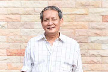 Portrait of smiling asian senior man standing in front of brick wall background with self confident manner. Closeup face of elder smile with gray hair.