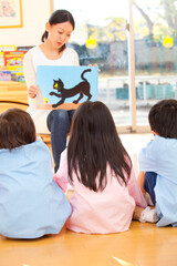 幼稚園児に紙芝居を読み聞かせる幼稚園教諭
