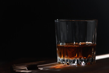 Glass of whiskey on dark wooden background with ray of light