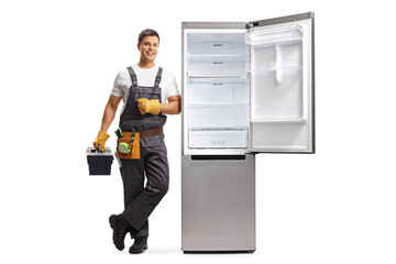 Full length portrait of a repairman with a tool box leaning on a fridge