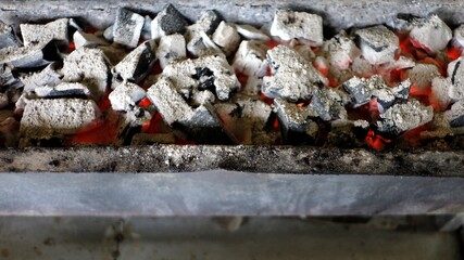 In selective focus firewood with hot coals from burning small wood logs in a stove 
