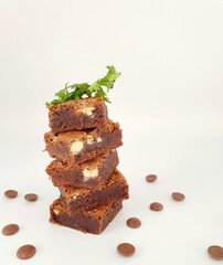 Chocolate brownies stacked with chocolate chips dispersed on a white background.