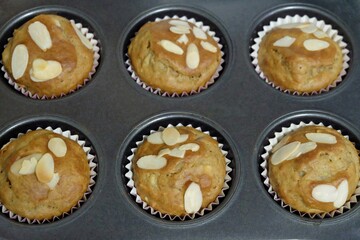 Close up homemade banana muffins in a black baking tray with almond sliced on top