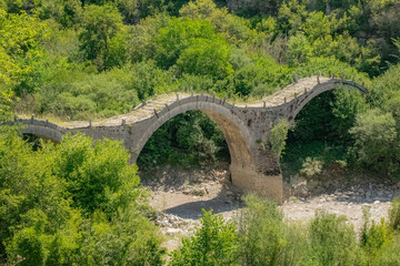 Fototapeta na wymiar Ancient amazing beautiful stone bridge of Kalogeriko with three arches over a river in Greece