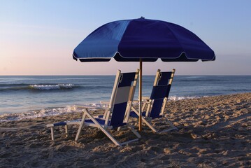 Lounge chairs under an umbrella on the beach at sunrise.