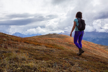 Fototapeta premium Adventurous Girl Hiking up the Nares Mountain during a cloudy and sunny evening. Taken at Carcross, near Whitehorse, Yukon, Canada.