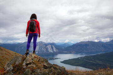 Naklejka premium Adventurous Girl Hiking up the Nares Mountain during a cloudy and sunny evening. Taken at Carcross, near Whitehorse, Yukon, Canada.